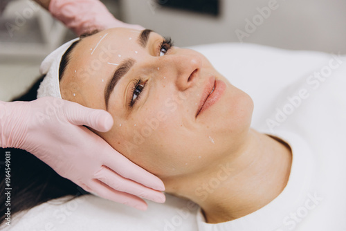 Woman receiving facial treatment with marked lines and dots for cosmetic procedure in beauty clinic