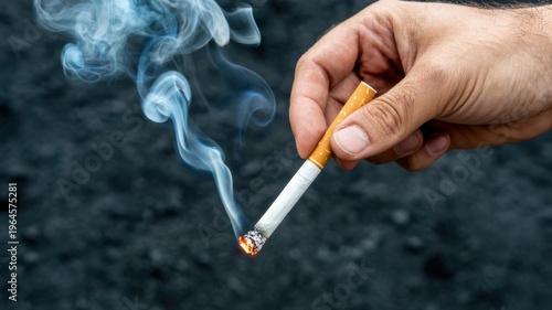 hand holding lit cigarette with smoke on dark background