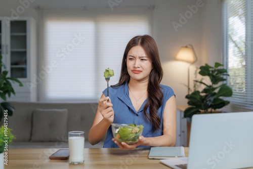 Young Asian woman feeling unhappy with her healthy diet, showing distaste for a bowl of fresh green vegetables