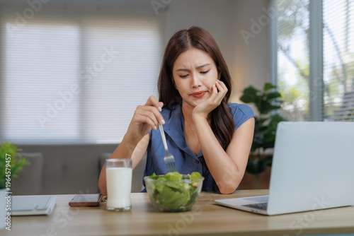 Bild auf Leinwand Young woman looking unhappy and bored while eating a bowl of green salad, doing