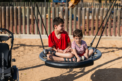 Brothers enjoying inclusive swing playing together in park