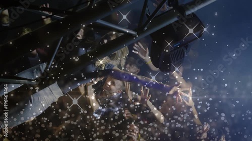 Attendees supporting crowd-surfer at music concert, arms rising, confetti falling, lights flaring