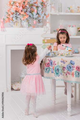 two little sisters celebrating easter at decorated table with eggs and sweets, cozy spring home scene with pastel colors and warm festive mood