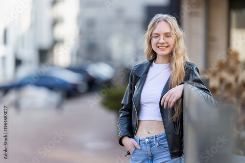 Young Woman Leaning on Railing in Leather Jacket Urban Casual Portrait With Glasses and Smile