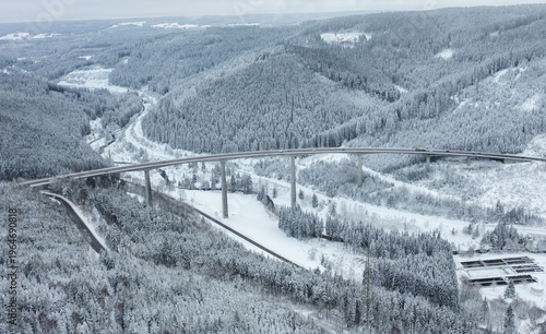 Drone aerial view of highway bridge with moving cars crossing a snowy forest valley in winter. Transportation and infrastructure in mountainous landscape of Black Forest, Germany