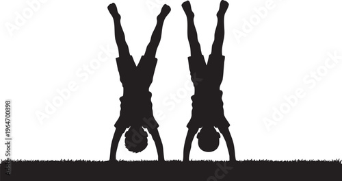Silhouettes of two playful children performing handstands on the grass, showcasing agility and balance