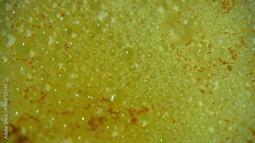 Extreme close up of a citrus flavored effervescent tablet dissolving in water, creating vibrant yellow bubbles foam

