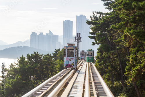Fotografie Colorful oceanfront capsule cars travel along an elevated coastal rail, offering scenic seaside views and a relaxed tourism experience over the water