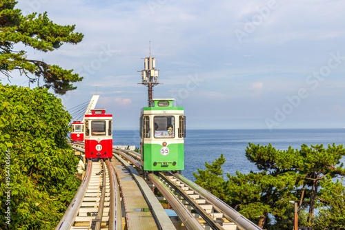 Photography Colorful oceanfront capsule cars travel along an elevated coastal rail, offering scenic seaside views and a relaxed tourism experience over the water