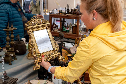 Принти на полотні A woman examines an ornate vintage mirror among assorted antiques and porcelain