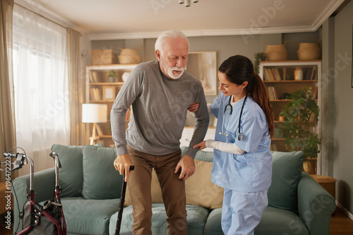 Fotografie Nurse helps older man use a cane while standing in his home