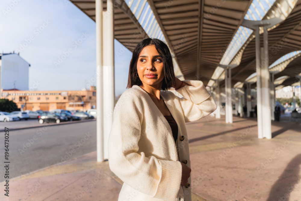 Obraz premium Young woman standing under modern architecture, looking back with natural light
