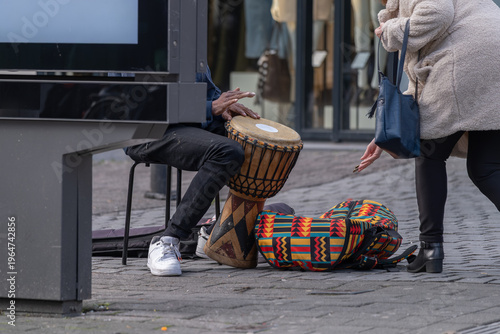 Street musician playing drum and receiving donation, urban busking and informal economy concept