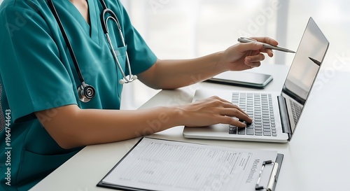 A healthcare professional in scrubs uses a laptop, pointing at the screen
