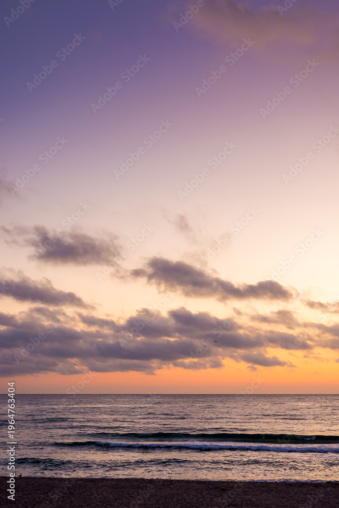 Fototapeta premium sunrise over the sea. beach landscape in golden glow. morning sky with purple clouds above horizon. scenery with calm waves. tranquil seascape wallpaper for summer vacation