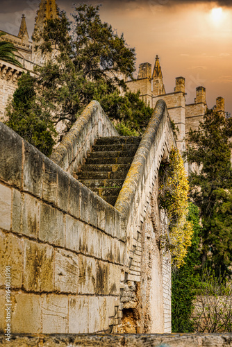 Escalera antigua de piedra hacia la Catedral de Palma de Mallorca bajo un cielo dorado al atardecer con arquitectura gótica majestuosa y atmósfera mística de viaje histórico y espiritualidad