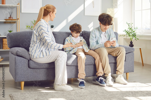Young mother arguing with her children sitting on sofa addicted from mobile phone. Kids using smartphone playing online game ignoring parent at home. Technology and gadgets addiction problem.