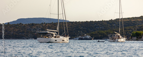Sailboats anchored calm sea bay mediterranean coast green hills clear sky during warm summer evening. Scenic marine landscape yachts travel leisure atmosphere tranquil seaside tourism destination