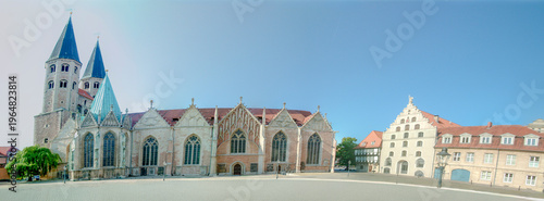 Vászonkép Panoramic view of a medieval church with twin spires and arched windows, adjacent to historic gabled buildings under a clear blue sky