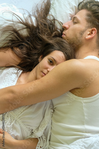 Young couple lying close together in bed tender embrace woman resting on partner chest soft light and natural tones create intimate calm atmosphere of trust and emotional connection