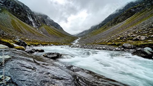 A serene mountain river flows through a rocky valley under a cloudy sky