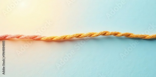 A single continuous braided rope, transitioning from light pink to golden yellow, lies elegantly on a pastel blue background, suggesting a conceptual representation of transformation and connection.