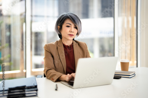 Smiling busy mature middle aged professional business woman manager executive wearing suit looking at laptop computer in office working at desk. Free Download Smiling busy mature middle aged professional business woman manager executive wearing suit looking at laptop computer in office working at desk. - GFXLoad