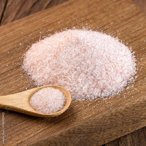 Wooden spoon with Himalayan pink salt on a wooden background, ideal for gourmet cooking and wellness concepts.
