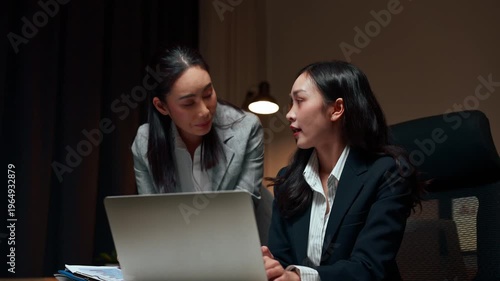 Two asian businesswomen collaborating on laptop at night
