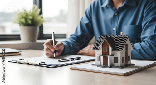 man signing documents for house loan at desk with miniature home model