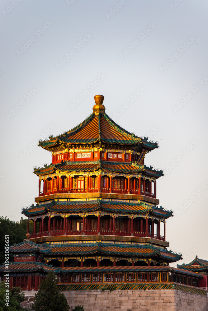 Obraz premium The Tower of Buddhist Incense (Foxiang Pavilion) at the Summer Palace in Beijing, China, rises above lush green trees under a clear summer sky.