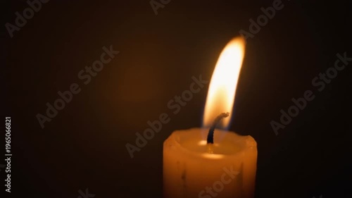 A burning candle glowing in the dark on a black background