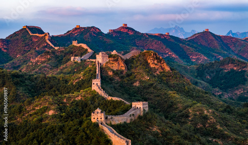 Jinshanling section of the Great Wall of China at sunset, with the ancient wall winding across mountain ridges under a glowing sky. 