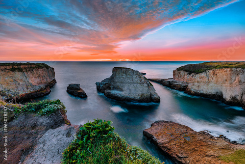 Shark Fin Cove along the California coast featuring dramatic layered rock formations and sea stacks rising from the Pacific Ocean. Long exposure captures smooth water and rugged coastal geology