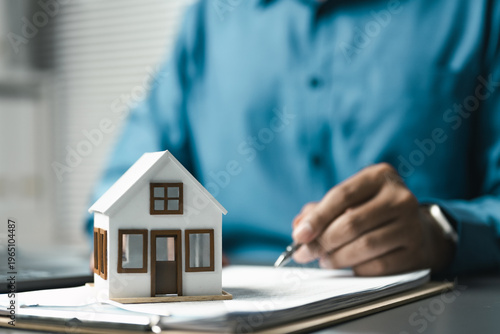 Obraz na płótnie Person signing real estate contract with house model, representing home purchase, property investment, mortgage agreement and financial approval