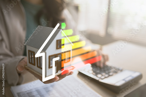 Photos Hand holding house model with energy efficiency rating scale, representing sustainable home, energy saving, cost reduction and environmental protection