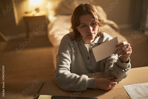 Bild auf Leinwand Young adult Caucasian woman sitting at desk holding photograph with thoughtful e