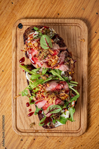 Delicious open-faced sandwich piled high with tender beef, greens, and a burst of flavor on a rustic wooden board