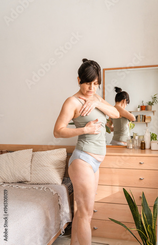 Adult woman checking her breasts for lumps, promoting areness and early detection of breast cancer at home. Taking care of your health and body
