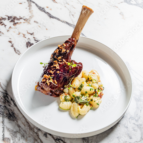 Fotografie Savory lamb shank served with creamy gnocchi and fresh herbs in a sophisticated