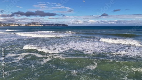 long rolling swells moving toward indistinct shoreline, calm sea rhythm, soft clouds, wide open horizon