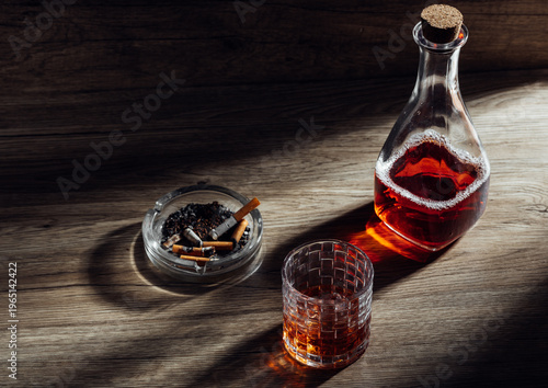 Glass decanter with whiskey, cigarette ashtray, and glass on wood