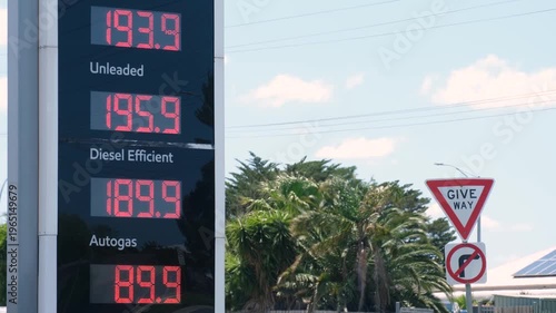 Fuel price board at a petrol station in Australia displaying unleaded, diesel, autogas prices, with roadside give way sign nearby. Rising fuel costs, transport expenses, car-dependent suburban life