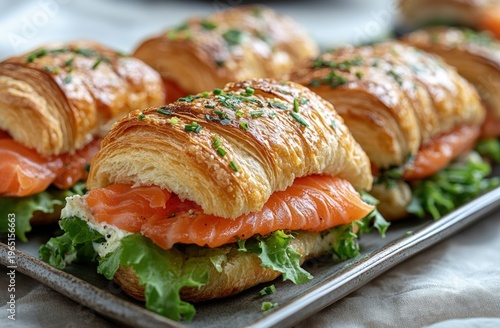 Golden croissants filled with smoked salmon, creamy spread, lettuce, and chives on a plate