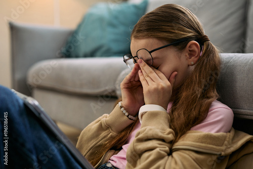 Foto Caucasian girl child sitting on floor rubbing eyes with both hands while wearing