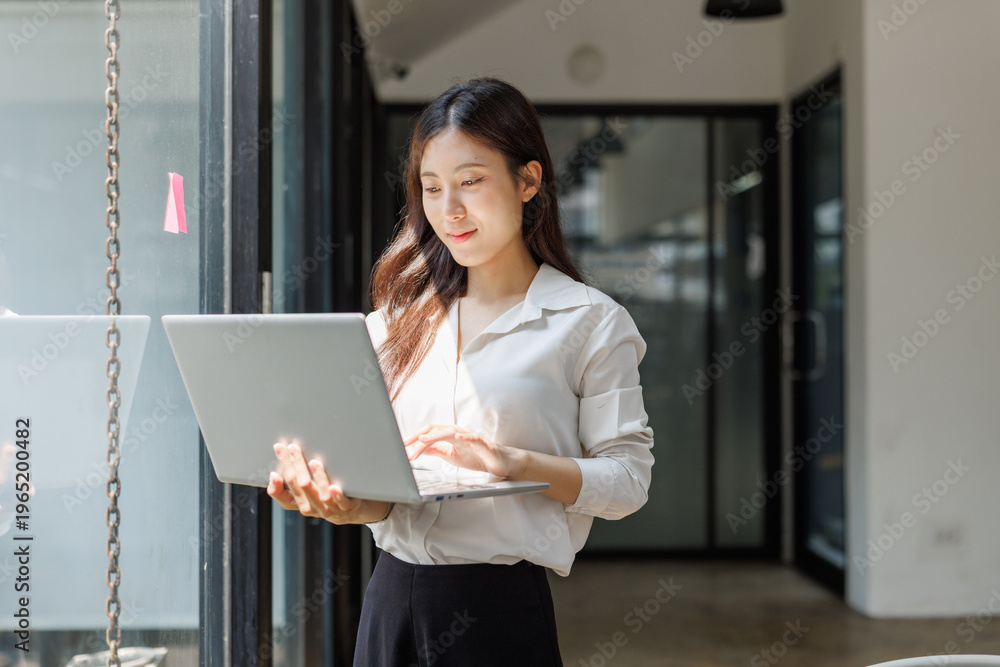 Fototapeta premium Young businesswoman standing typing on laptop workspace