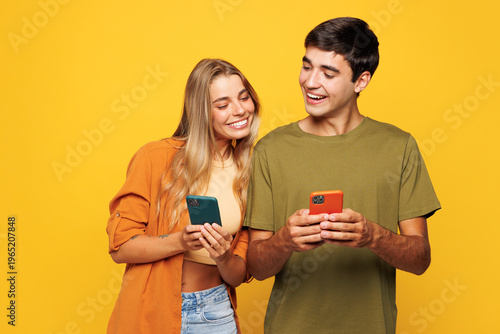 Young smiling happy satisfied couple friends family man woman wear casual clothes hold in hand use mobile cell phone together isolated on pastel plain light yellow color background studio portrait