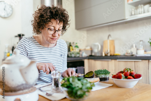 Foto Middle aged woman preparing healthy breakfast with avocado and greens