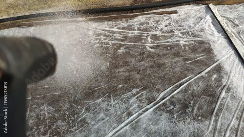 Hand holding watering nozzle spraying water on white canvas covering freshly sown grass seeds in garden. Lawn care and landscaping concept.
