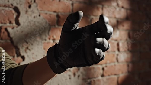A close-up shot of a gloved hand making a fist in front of a dimly lit brick wall during a police raid operation.